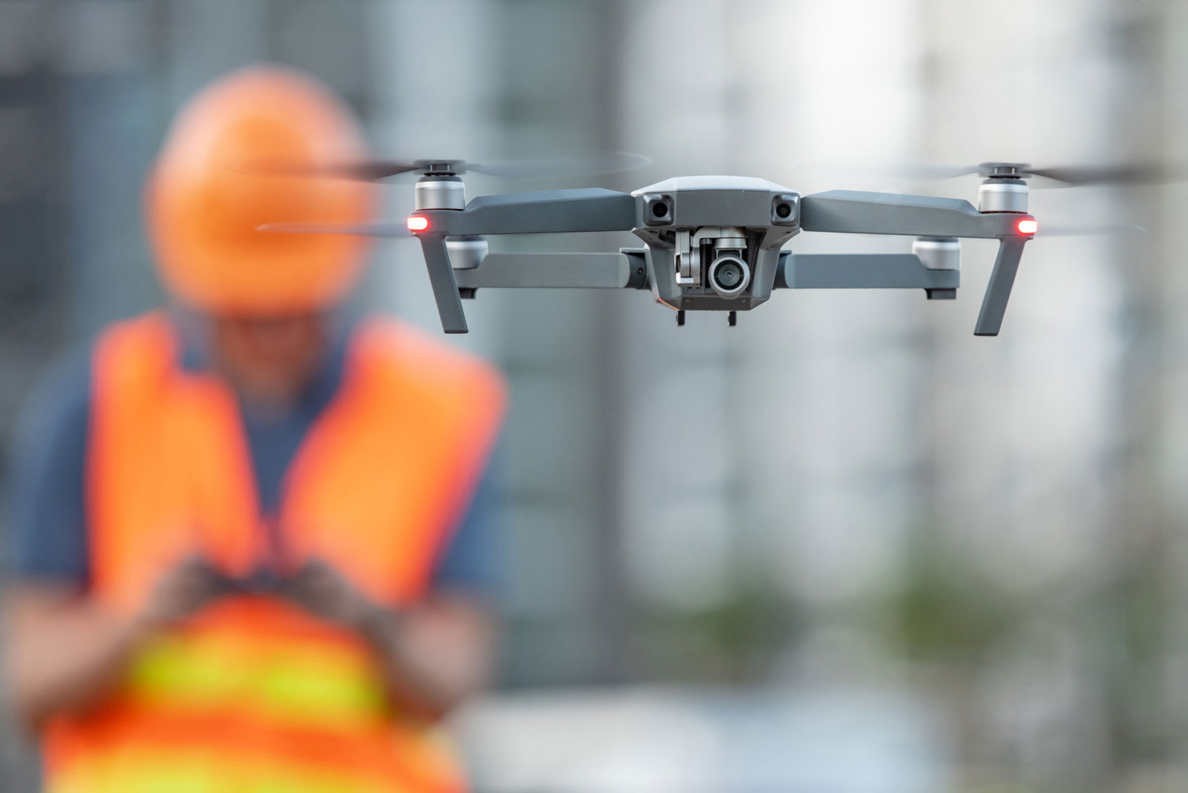 A drone hovering close to the camera with an operator controlling it in the background.