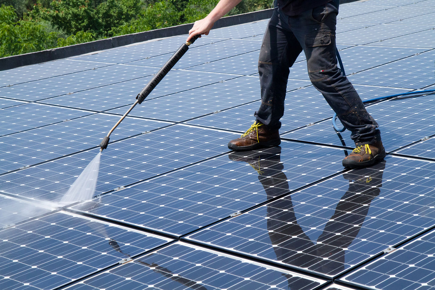 A man pressure washing a large collection of solar panels.